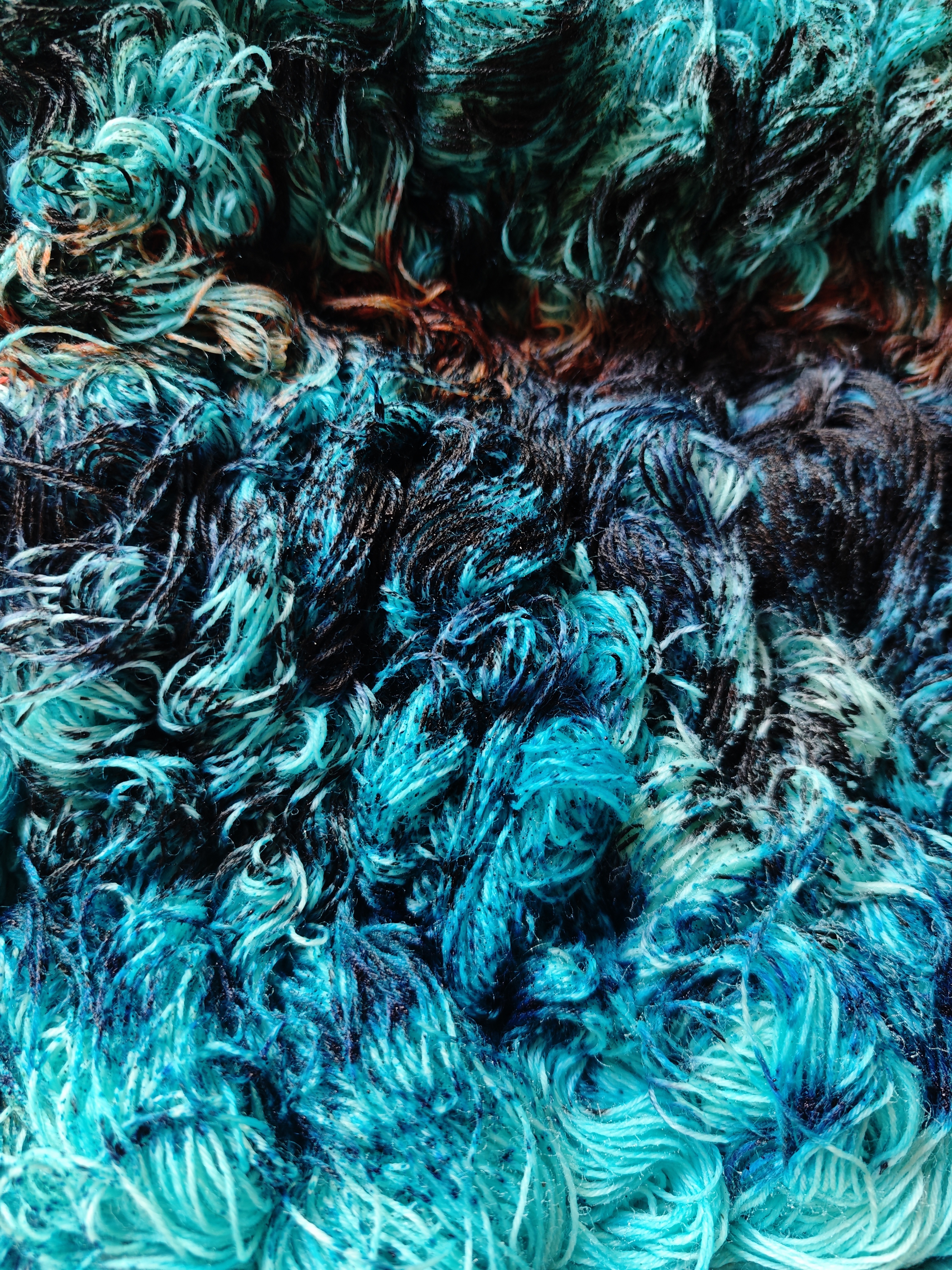 Un mar de lana azul turquesa con manchas oscuras, verdes, negras y naranjas