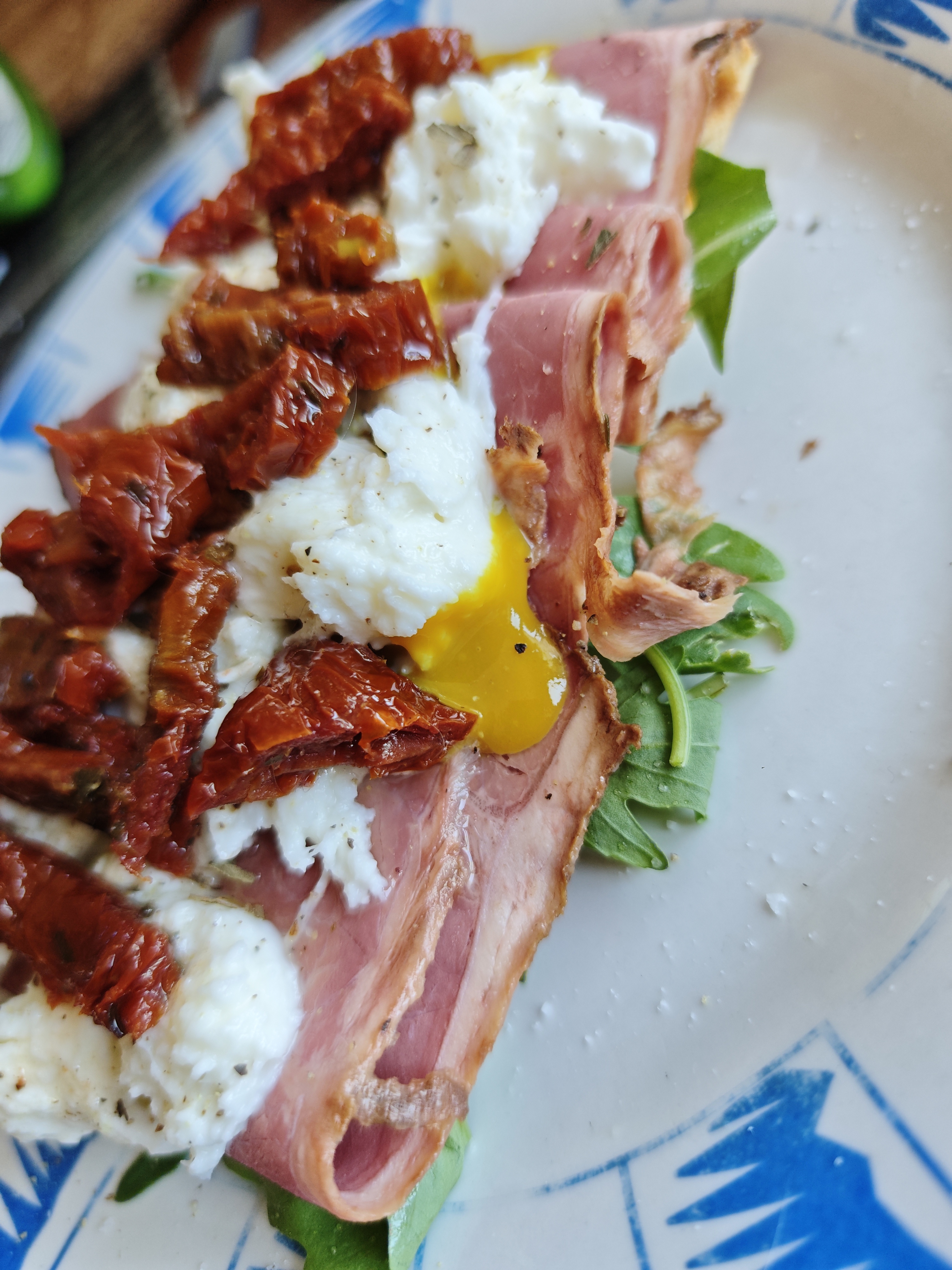 Una tosta de pan con rúcula, pastrami, salsa de mostaza, mozzarella y tomate seco en aceite de oliva