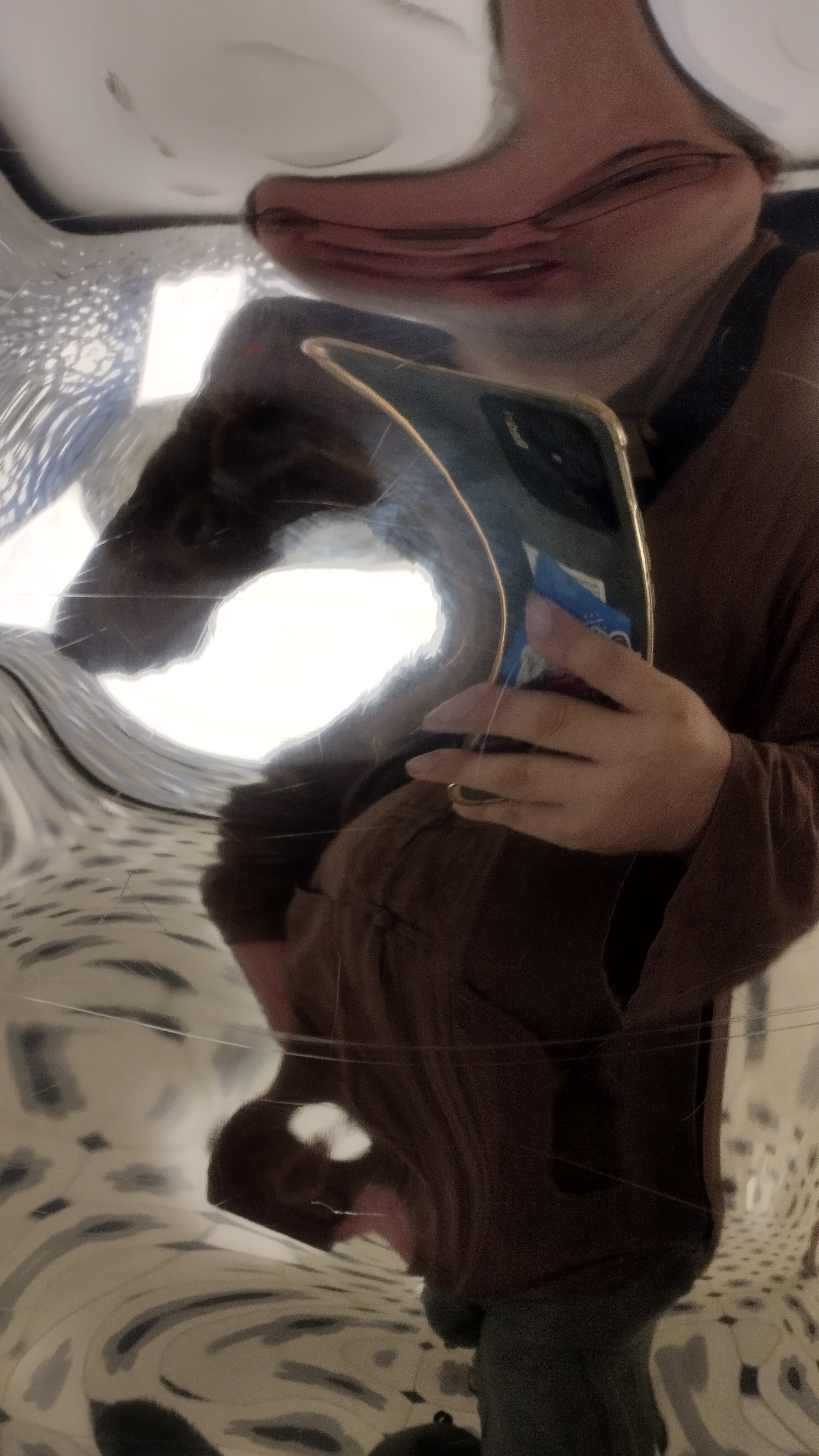 autorretrato de una persona con gafas delante de  un espejo que deforma mucho. parece que tengo tres ojos y se ve mi mano con un teléfono muy deformado. se ve también que llevo una camisa marrón