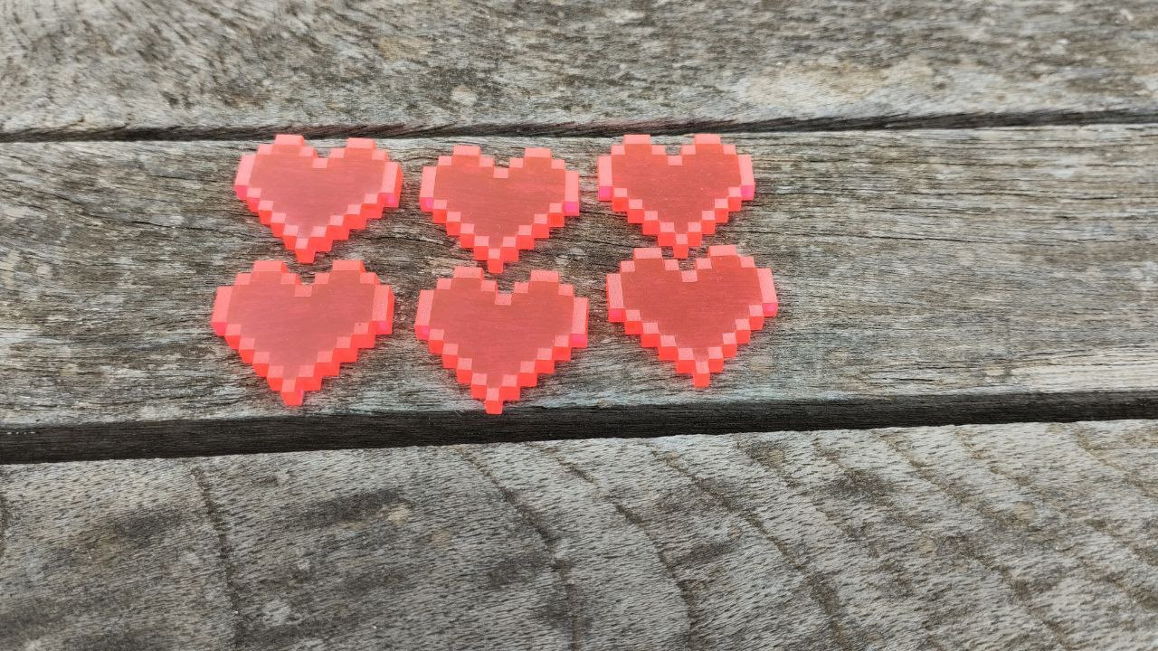 6 tokens de metacrilato con forma de corazones pixelados sobre un fondo de madera. Estos son los de "dieciséis bits"