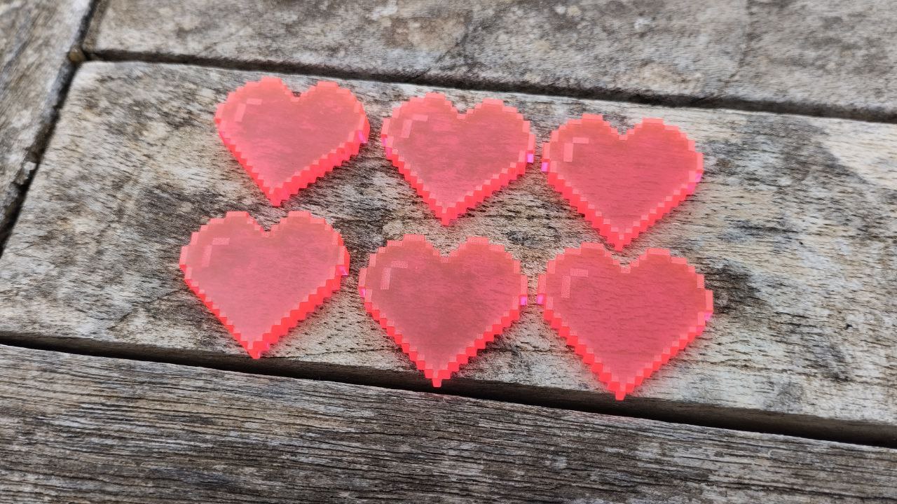 6 tokens de metacrilato con forma de corazones pixelados sobre un fondo de madera. Estos son los de "ocho bits"